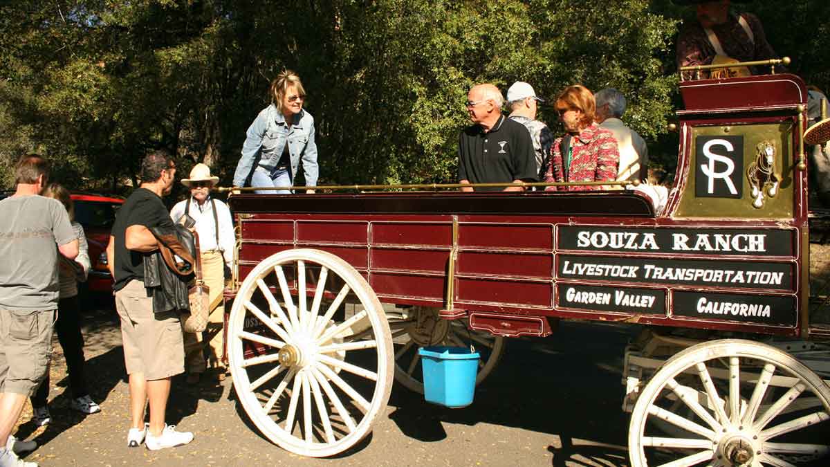 A group of people getting into red wagon with large, white, wooden wheels.