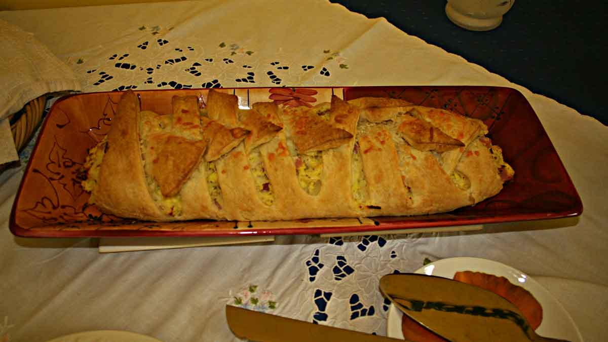 A baked ham & egg breakfast pastry served on a large, long orange and brown glass tray.
