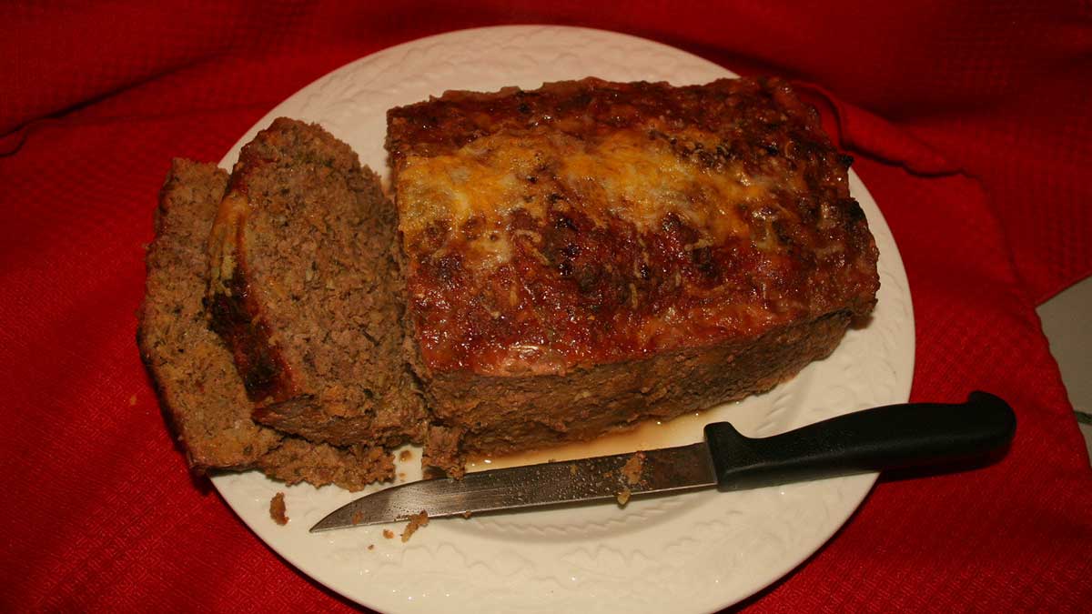 Freshly baked meatloaf cut into slices on a white plate atop a red tablecloth.