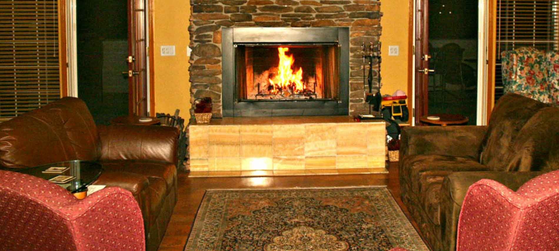 A large yellow colored room with a fireplace burning, two love seats facing each other and two chairs