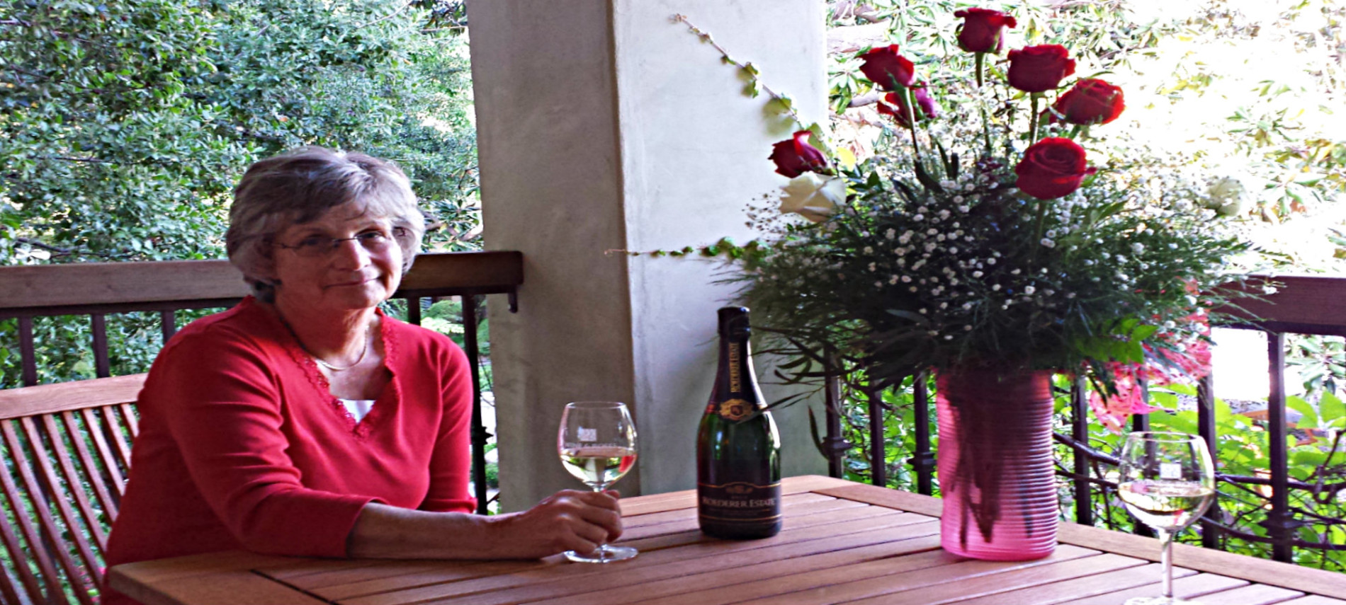 Lucinda in a red blouse, sitting at a wood table by a bouquet of red and white roses.