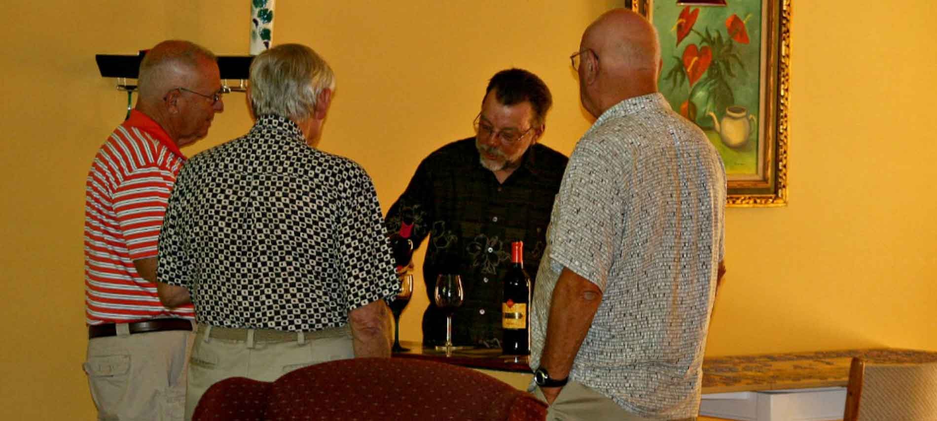 Three men standing with back to camera with a man pouring wine in a yellow colored room