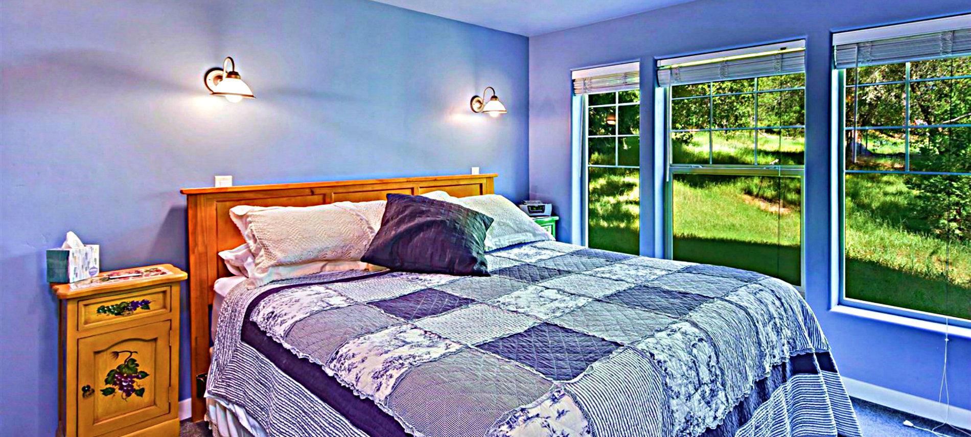 Bed with white & pink spread with several shaped pillows and tables on each side and a blue wall