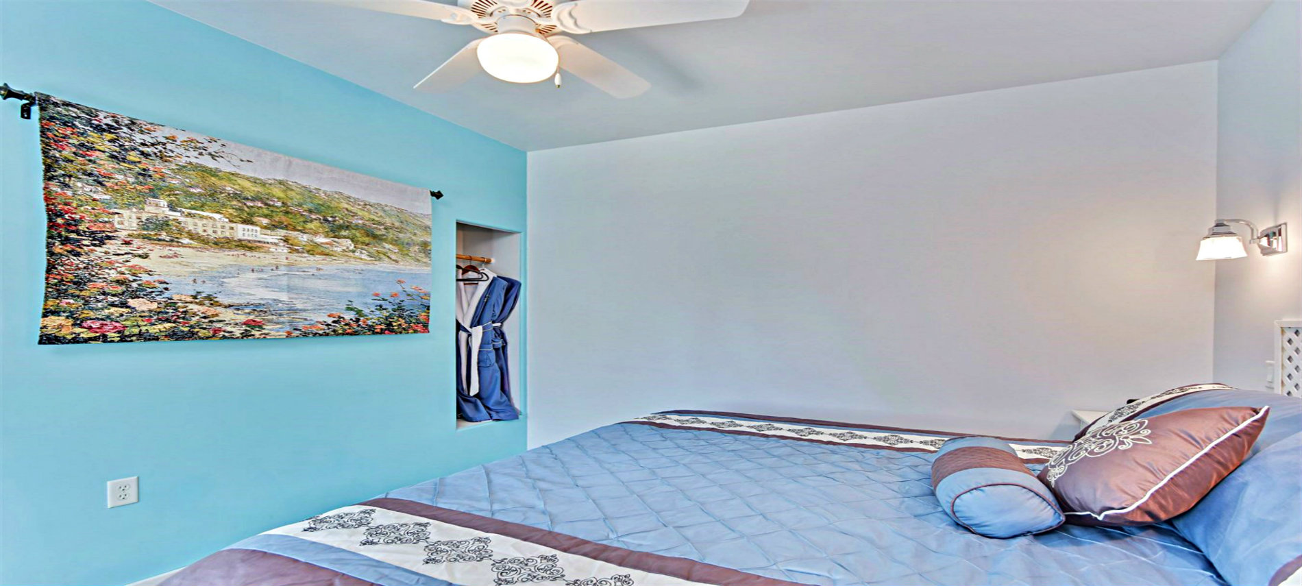 Bed with Multi-colored Spread and Pillows at the Head of the Bed and Two White Tables