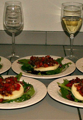 Several white plates with salad greens, big slices of white cheese and tomato relish.